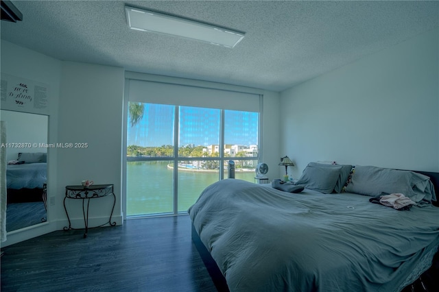 bedroom with a water view, dark hardwood / wood-style floors, and a textured ceiling