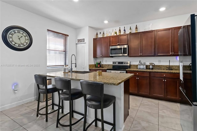 kitchen featuring sink, a breakfast bar area, appliances with stainless steel finishes, dark stone counters, and a kitchen island with sink