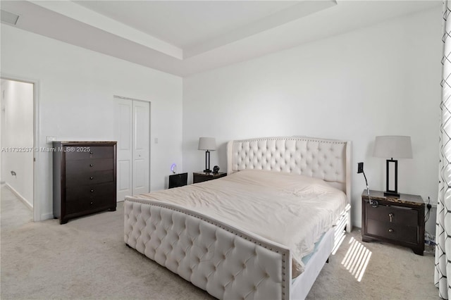 bedroom featuring a tray ceiling, light carpet, and a closet