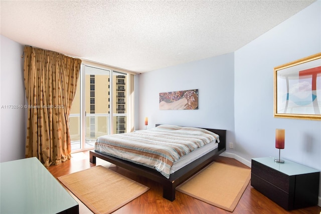 bedroom with access to exterior, hardwood / wood-style flooring, expansive windows, and a textured ceiling