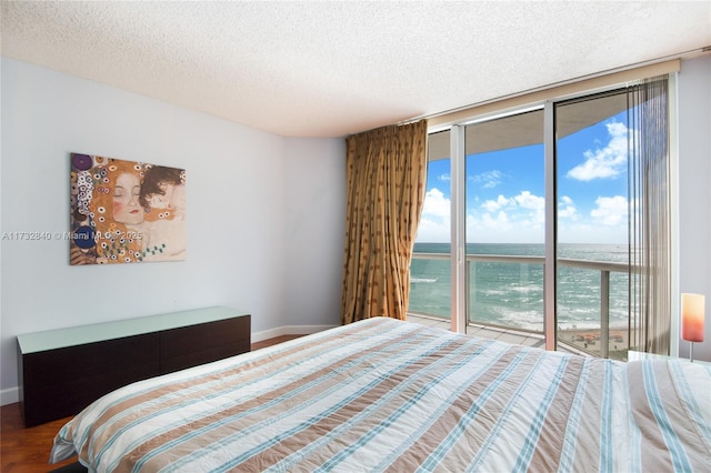 bedroom with access to outside, expansive windows, a textured ceiling, and a water view