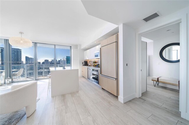 kitchen with pendant lighting, expansive windows, a center island, stainless steel oven, and paneled fridge