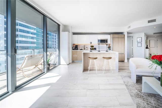 kitchen featuring a breakfast bar, white cabinets, a wall of windows, a kitchen island with sink, and paneled built in fridge