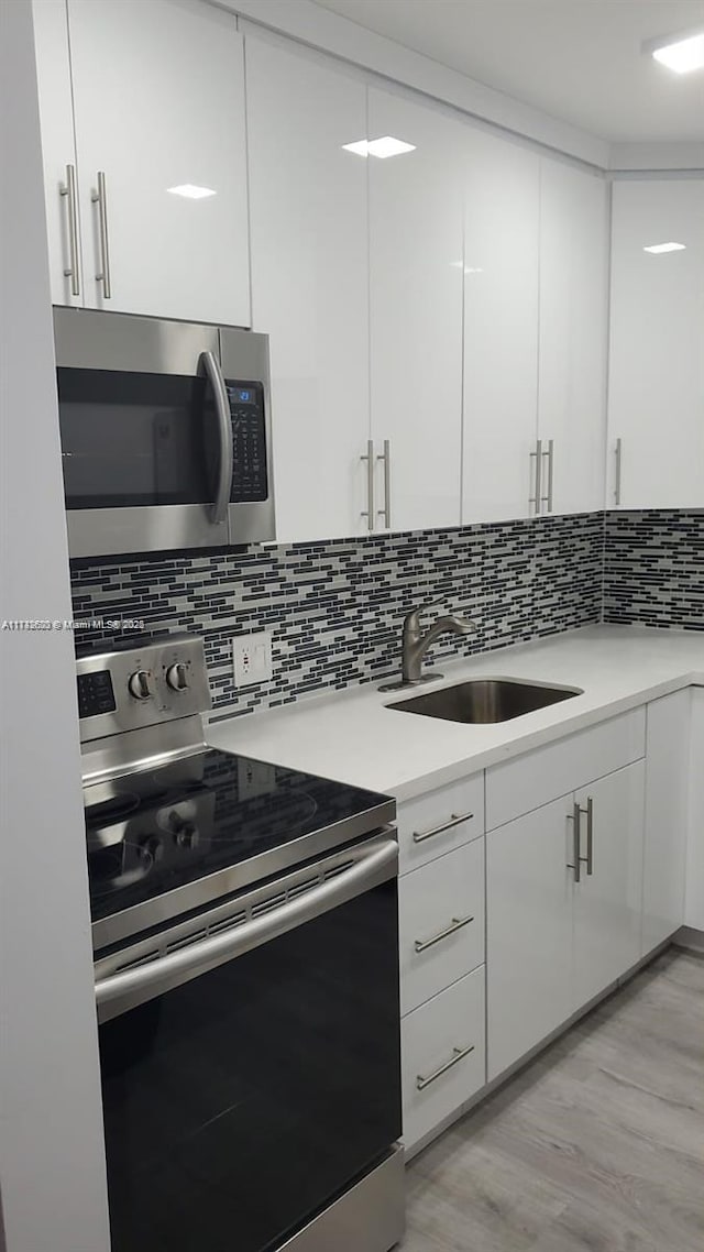 kitchen featuring sink, light wood-type flooring, appliances with stainless steel finishes, decorative backsplash, and white cabinets