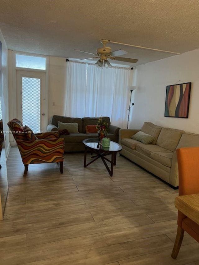 living room with ceiling fan, a textured ceiling, and light wood-type flooring