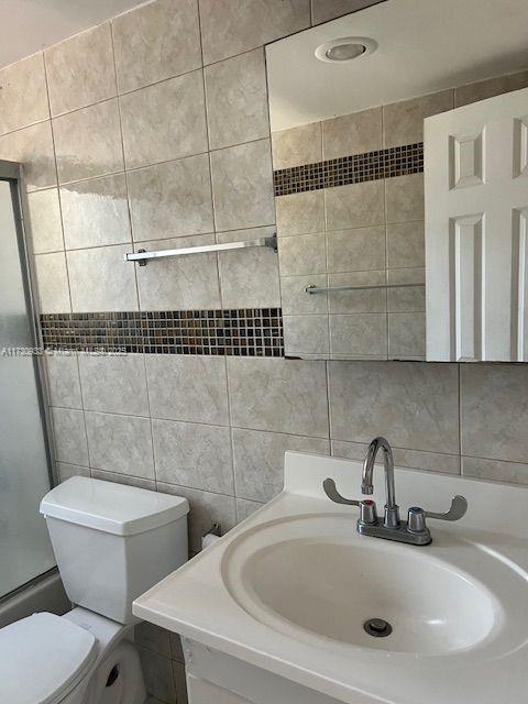 full bathroom with tile walls, tasteful backsplash, shower / bath combination with glass door, and toilet