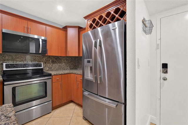 kitchen with stainless steel appliances, light tile patterned floors, dark stone counters, and decorative backsplash