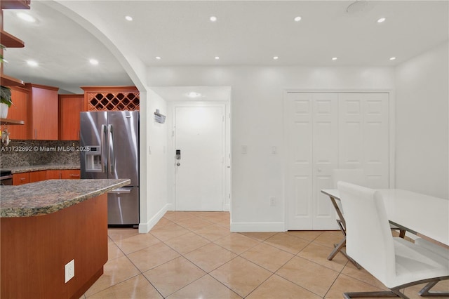 kitchen with light tile patterned floors, backsplash, dark stone counters, and stainless steel refrigerator with ice dispenser