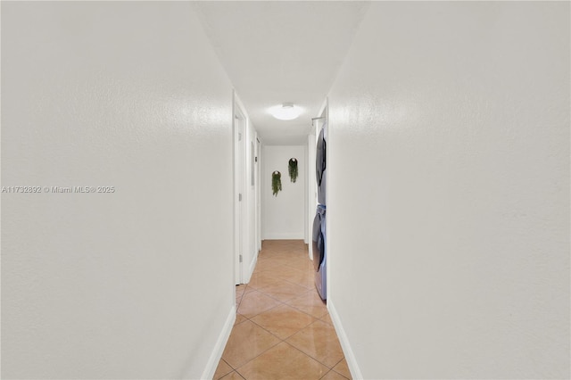 hall with stacked washer / dryer and light tile patterned flooring