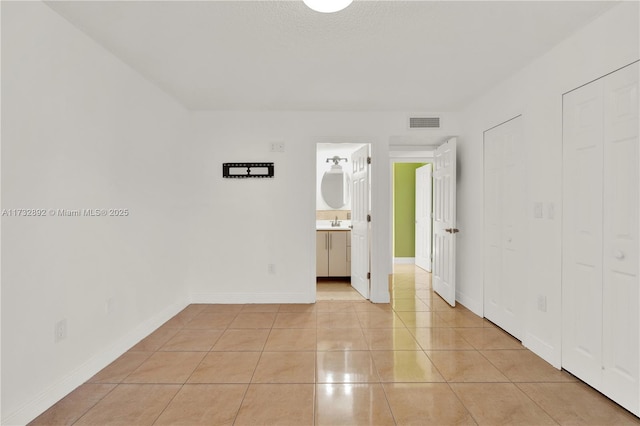 unfurnished bedroom with light tile patterned floors, ensuite bath, and sink