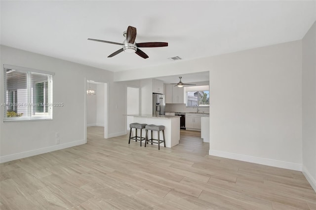 unfurnished living room featuring ceiling fan with notable chandelier, light hardwood / wood-style floors, and sink