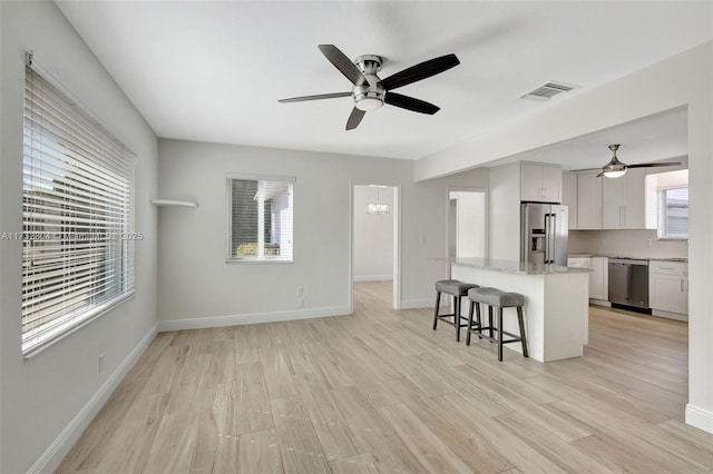 kitchen featuring white cabinetry, light wood-type flooring, appliances with stainless steel finishes, a kitchen breakfast bar, and ceiling fan with notable chandelier