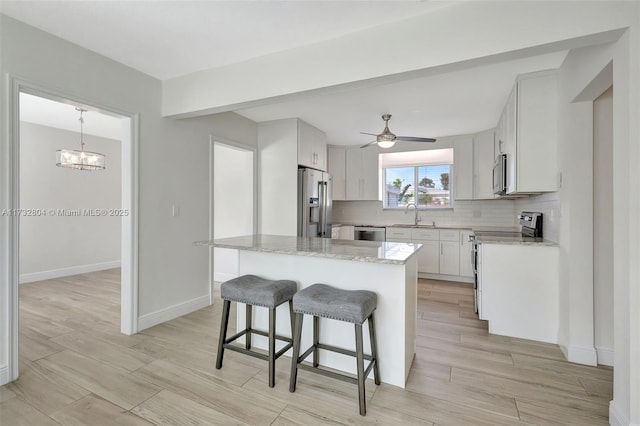 kitchen featuring sink, stainless steel appliances, white cabinets, a kitchen island, and decorative light fixtures