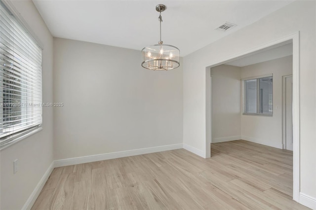 spare room featuring a wealth of natural light, a notable chandelier, and light hardwood / wood-style flooring