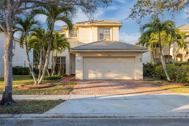 mediterranean / spanish-style house featuring an attached garage, a tile roof, decorative driveway, and stucco siding