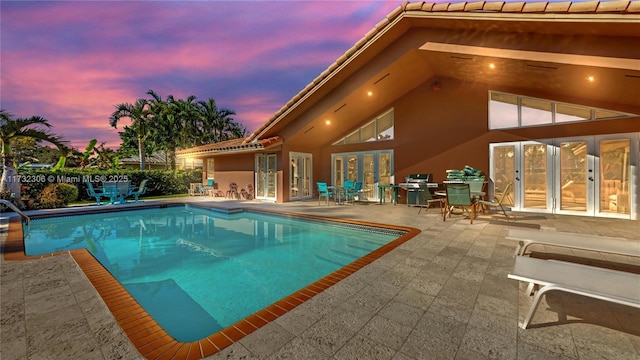 pool at dusk featuring a patio and french doors