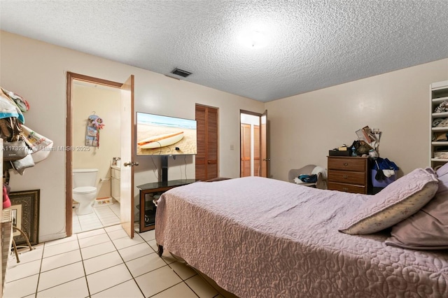 bedroom featuring connected bathroom, a textured ceiling, and light tile patterned floors