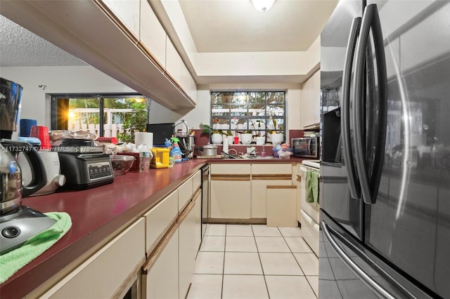 kitchen featuring light tile patterned floors, sink, appliances with stainless steel finishes, cream cabinets, and a textured ceiling