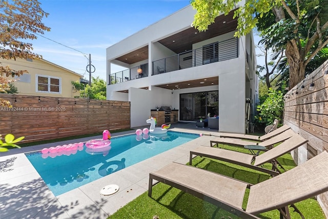 back of property with an outdoor kitchen, a fenced in pool, a balcony, and a patio area