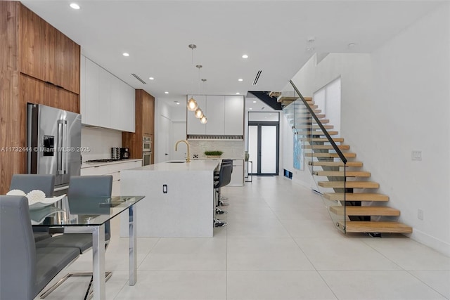 kitchen with appliances with stainless steel finishes, decorative light fixtures, an island with sink, sink, and white cabinets