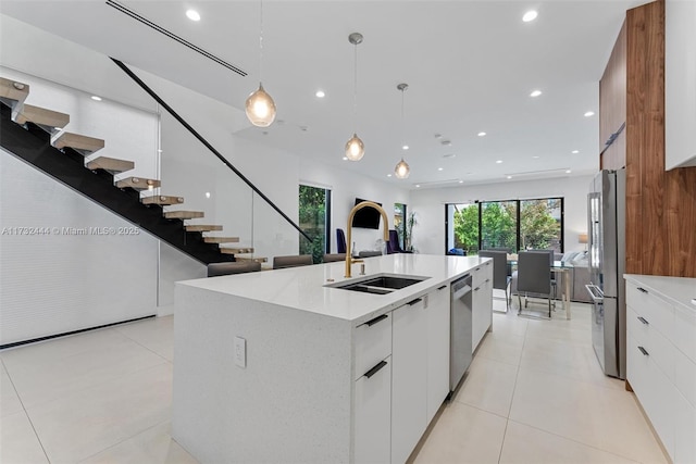 kitchen featuring sink, appliances with stainless steel finishes, white cabinetry, hanging light fixtures, and a center island with sink