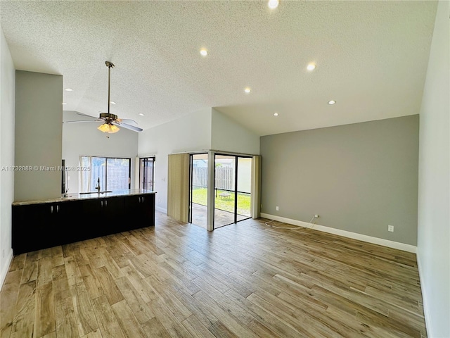 unfurnished living room featuring ceiling fan, high vaulted ceiling, a textured ceiling, and light wood-type flooring