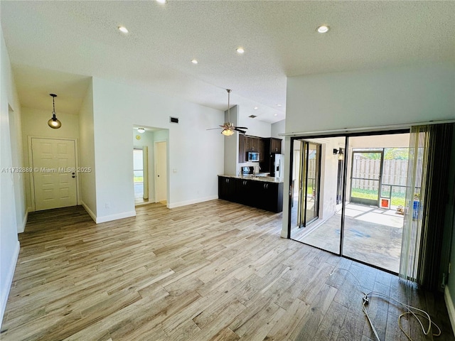 unfurnished living room with ceiling fan, high vaulted ceiling, light hardwood / wood-style floors, and a textured ceiling