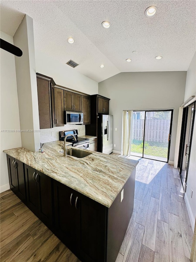 kitchen with lofted ceiling, sink, light wood-type flooring, kitchen peninsula, and stainless steel appliances