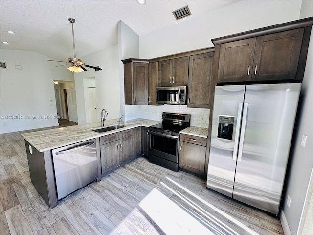 kitchen featuring sink, stainless steel appliances, tasteful backsplash, vaulted ceiling, and kitchen peninsula