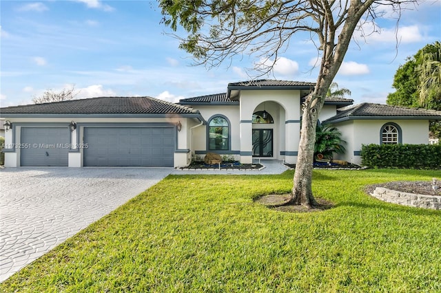 mediterranean / spanish-style home featuring an attached garage, a tiled roof, decorative driveway, stucco siding, and a front yard