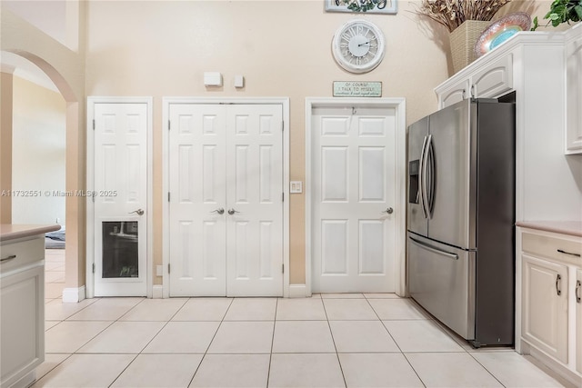 kitchen featuring light tile patterned floors, arched walkways, white cabinets, light countertops, and stainless steel fridge with ice dispenser