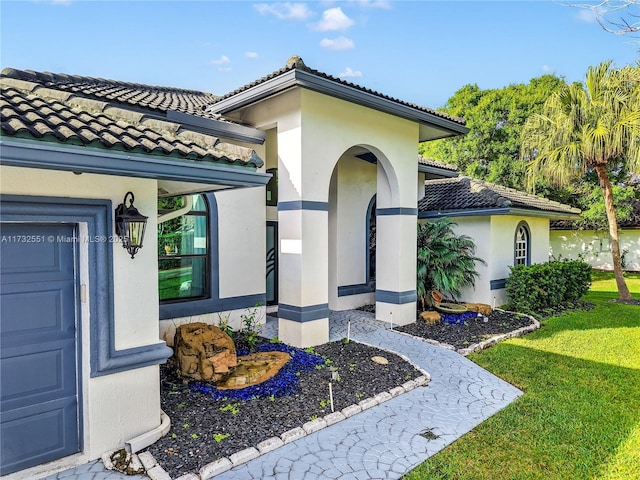 property entrance featuring a lawn, a tiled roof, an attached garage, and stucco siding