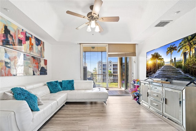 living room with ceiling fan, a raised ceiling, and light hardwood / wood-style flooring