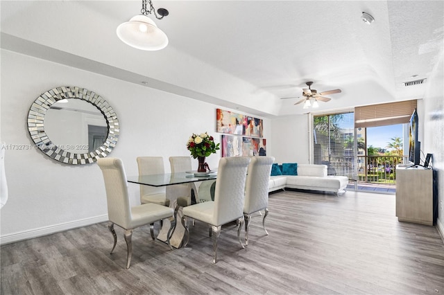 dining area featuring ceiling fan, a tray ceiling, wood-type flooring, and a textured ceiling