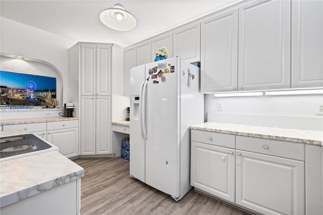 kitchen featuring lofted ceiling, light hardwood / wood-style floors, white fridge with ice dispenser, white cabinets, and a textured ceiling