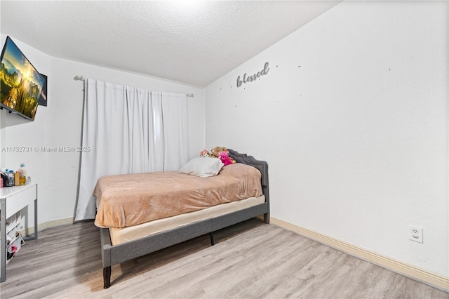 bedroom with vaulted ceiling, light hardwood / wood-style floors, and a textured ceiling