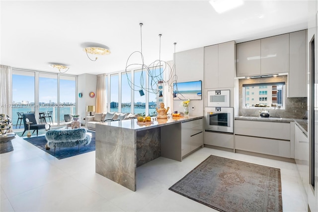 kitchen featuring tasteful backsplash, a wall of windows, a water view, and gray cabinets