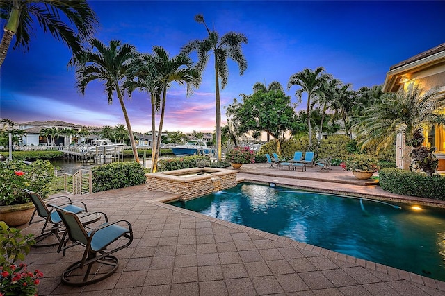 pool at dusk with an in ground hot tub, a water view, and a patio area