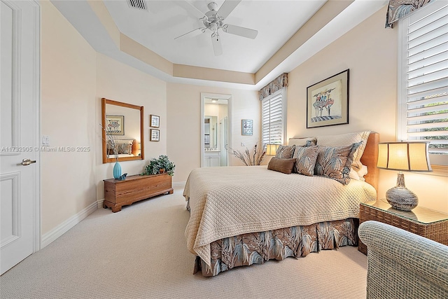 bedroom with ceiling fan, ensuite bathroom, a tray ceiling, and carpet floors