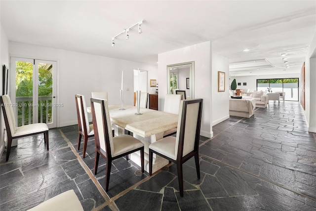 dining space with track lighting, stone tile flooring, and baseboards