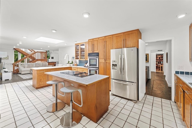 kitchen featuring a peninsula, a skylight, appliances with stainless steel finishes, tile counters, and glass insert cabinets