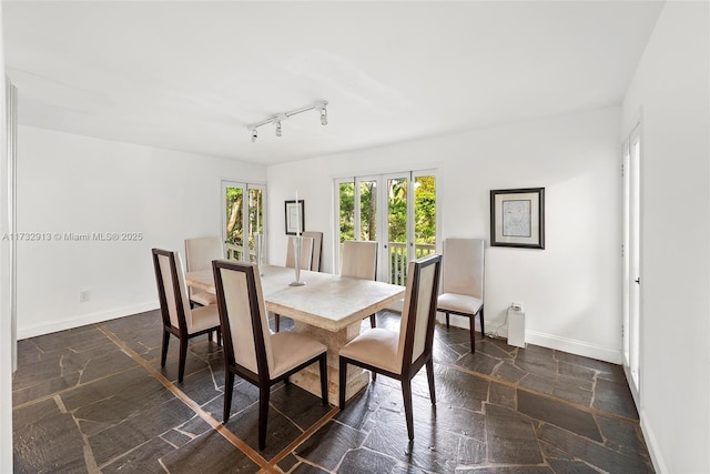 dining space with baseboards, track lighting, and stone tile floors