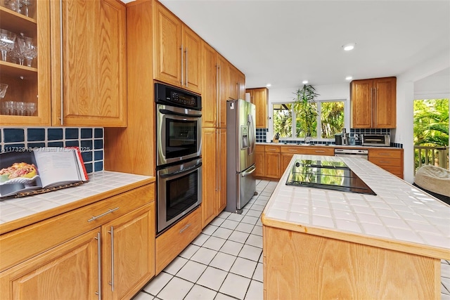 kitchen with decorative backsplash, tile countertops, appliances with stainless steel finishes, a center island, and light tile patterned flooring