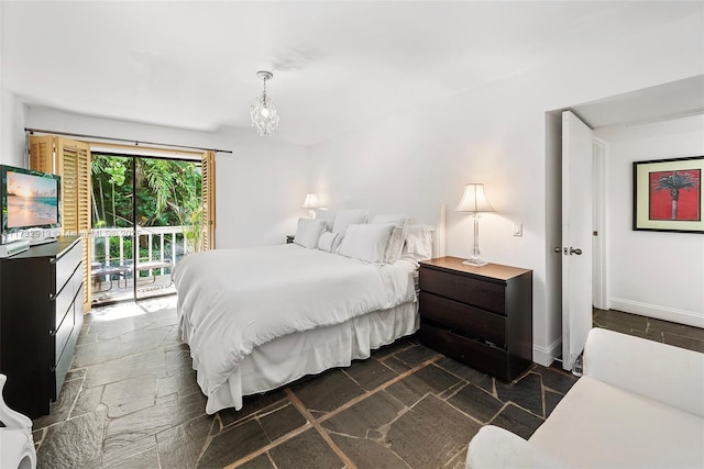 bedroom with baseboards, an inviting chandelier, stone tile flooring, and access to exterior