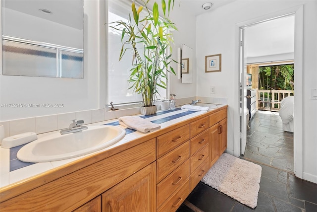ensuite bathroom with double vanity, stone tile floors, connected bathroom, and a sink