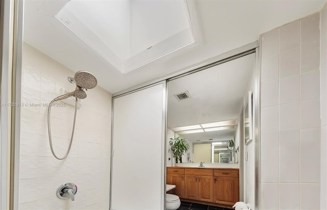 bathroom featuring toilet, tiled shower, visible vents, and tile walls