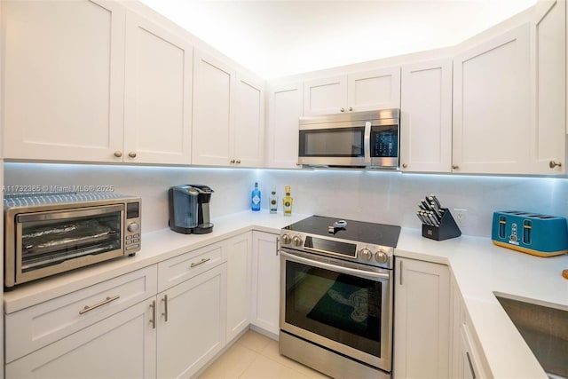 kitchen with appliances with stainless steel finishes, sink, light tile patterned floors, and white cabinets