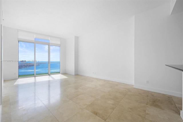 empty room featuring expansive windows, a water view, baseboards, and light tile patterned floors