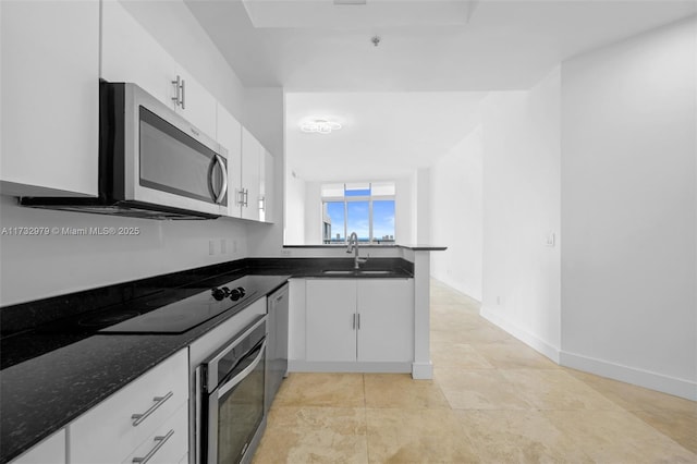 kitchen with white cabinets, stainless steel appliances, a sink, dark stone counters, and light tile patterned floors