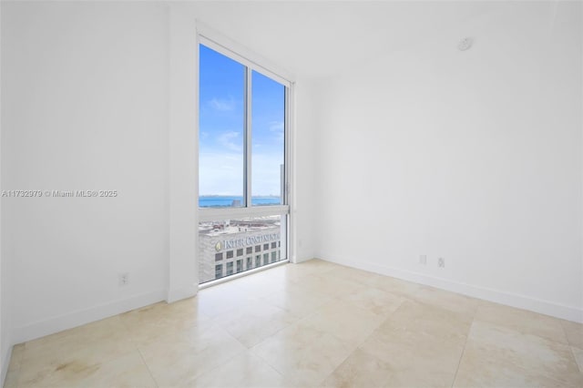 tiled empty room featuring baseboards and a water view